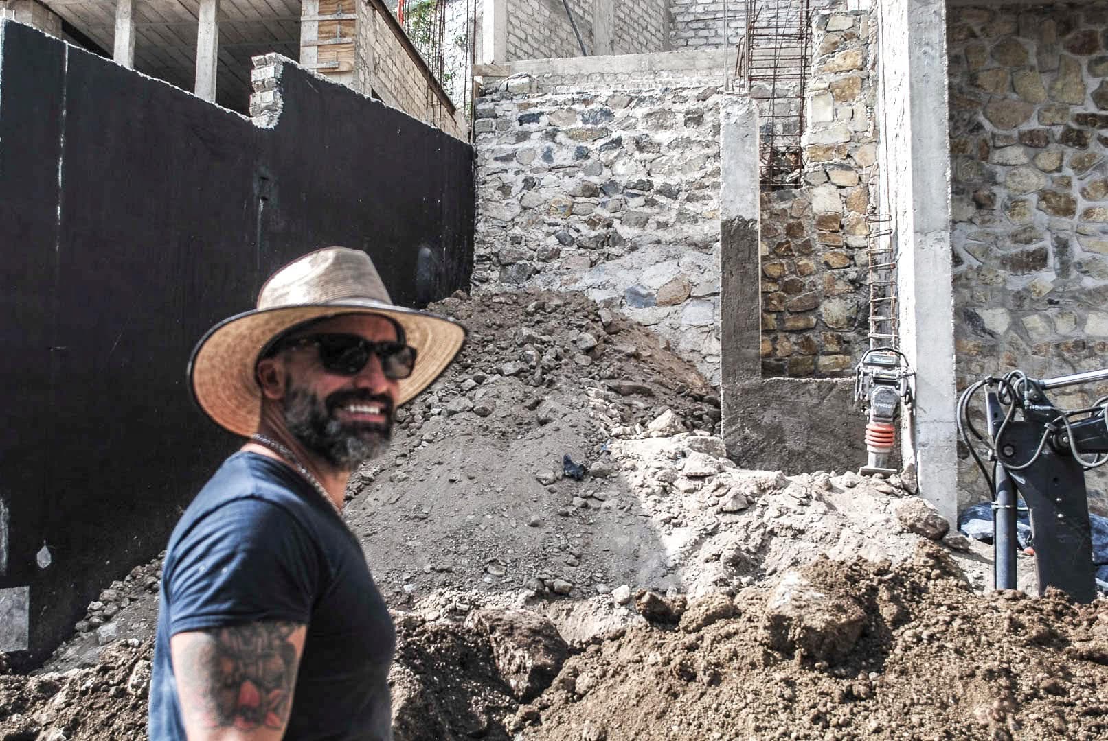 The builder on a job site near Lake Chapala in a straw hat, smiling, with stone walls going up behind him